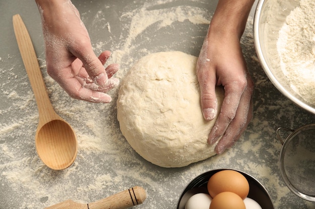 Mains mâles pétrir la pâte sur saupoudré de gros plan de table de farine