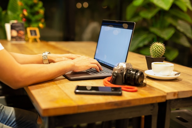 Mains mâles travaillant sur ordinateur portable avec caméra et café sur la table.