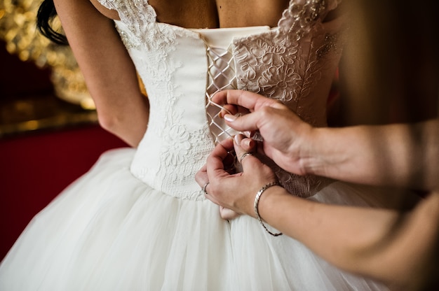 Les mains de maman nouent le corset de la robe de mariée de la mariée