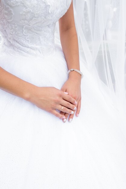 Mains de mariée avec bague de mariage sur le doigt sur le fond de la robe de mariée.