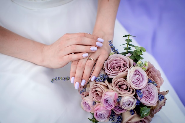 Les mains de la mariée à côté du bouquet sur le fond de la robe de mariée