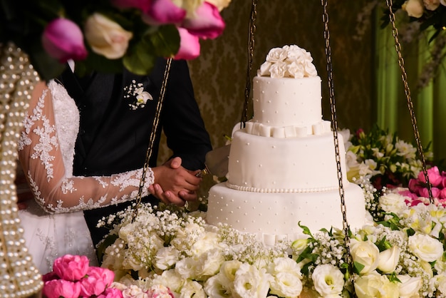 Les mains de la mariée et du marié découpent un gâteau de mariage.