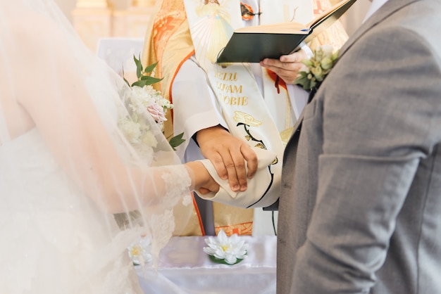 Photo mains de la mariée et du marié et du gros plan du prêtre. le sacrement du mariage dans l'église