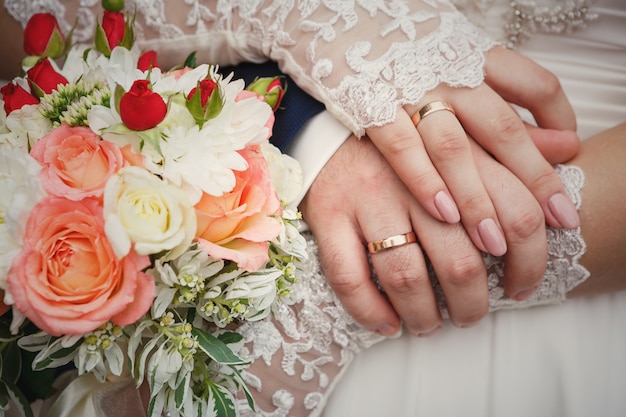 Mains de la mariée et le marié avec bouquet de mariage et bagues