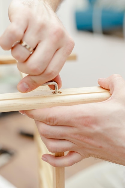 Les mains masculines assemblent des meubles en bois en serrant la vis avec un tournevis en métal