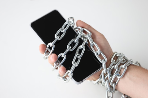 Les mains masculines attachées avec une chaîne et tenant la dépendance du smartphone aux gadgets modernes et aux réseaux sociaux