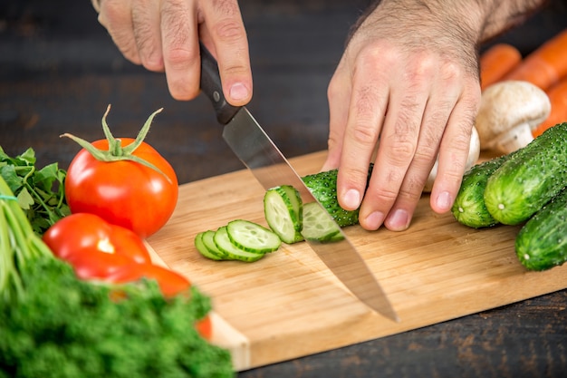 Mains masculines coupant des légumes pour la salade
