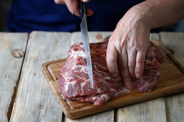 Les mains masculines avec un couteau ont coupé la viande crue sur le conseil