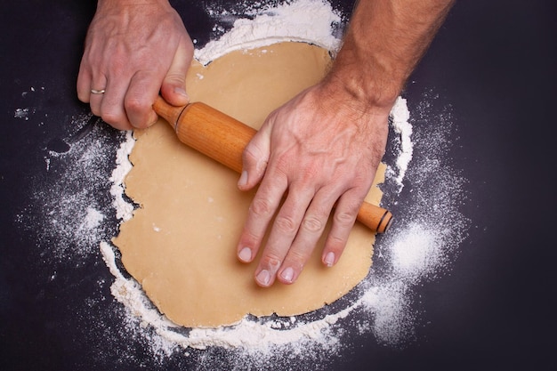 Des mains masculines étalent la pâte sur une table noire. Vue d'en-haut. Notion de Noël