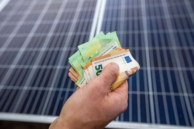 Mains masculines fortes d'un travailleur détenant des billets en euros pour le travail effectué Le concept de paiement pour l'installation de panneaux solaires