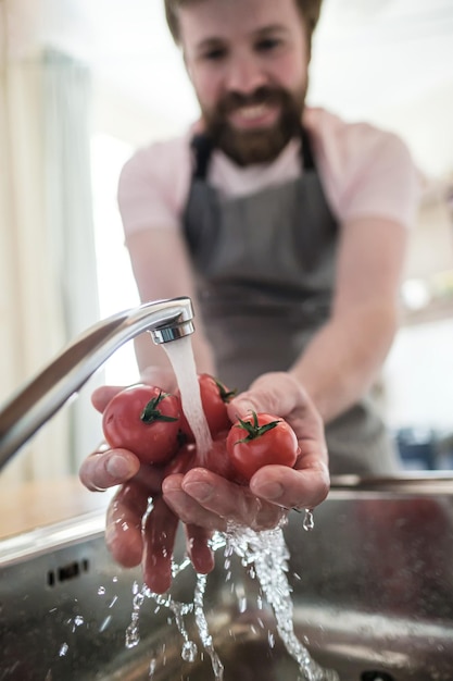Photo les mains masculines lavent les tomates rouges sous l'eau courante dans un évier