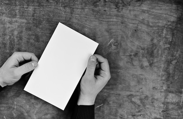 Mains masculines tenant une feuille de papier vierge blanche sur le fond de la table de texture en bois