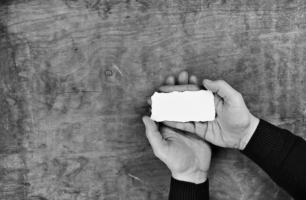 Mains masculines tenant une feuille de papier vierge blanche sur le fond de la table de texture en bois