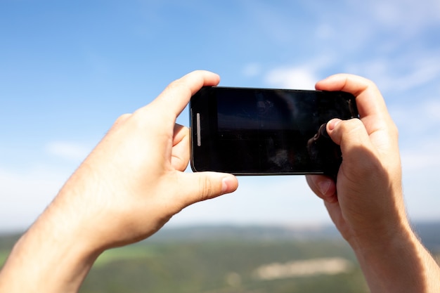 Des mains masculines tenant son téléphone portable à l'extérieur, enregistrent une vidéo dans le parc paysager