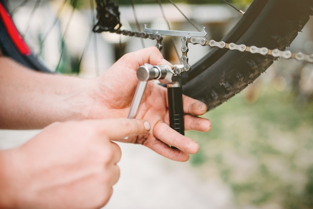 Les mains de mécanicien de vélo ajuste la chaîne de vélo avec des outils de service.