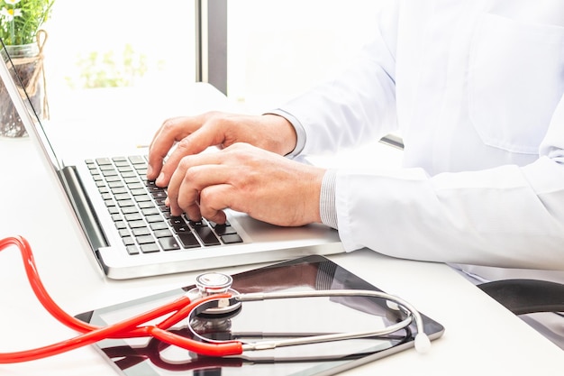 Mains d'un médecin en blouse blanche dont le visage n'est pas reconnu en train de taper sur le clavier d'un ordinateur portable