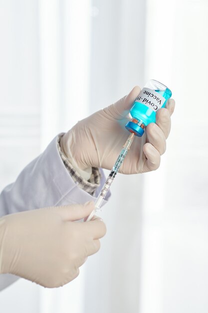 Mains de médecin dans des gants de protection se préparant à injecter un vaccin contre le coronavirus à partir d'un flacon en verre