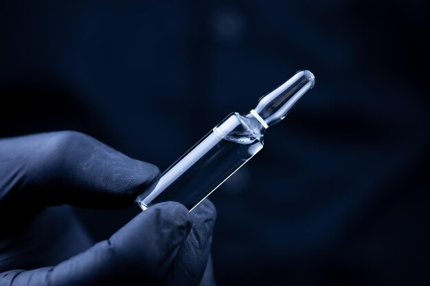 Les mains d'un médecin en gants médicaux noirs qui retourne une ampoule avec un vaccin