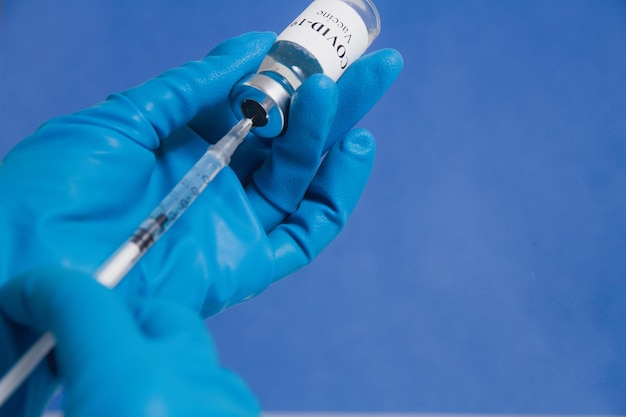 Mains d'un médecin ou d'une infirmière en gants médicaux bleus dessinant une seringue avec le vaccin covid19 à partir d'un espace de copie de flacon en gros plan Concept de vaccination contre le coronavirus