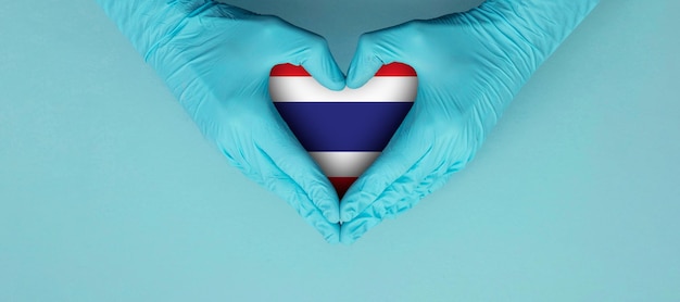 Les mains des médecins portant des gants chirurgicaux bleus faisant entendre le symbole de la forme avec le drapeau de la thaïlande