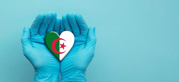 Mains de médecins portant des gants chirurgicaux tenant le coeur du drapeau algérien