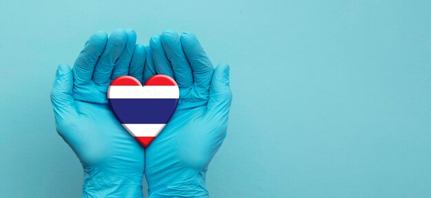 Mains de médecins portant des gants chirurgicaux tenant le coeur du drapeau de la thaïlande