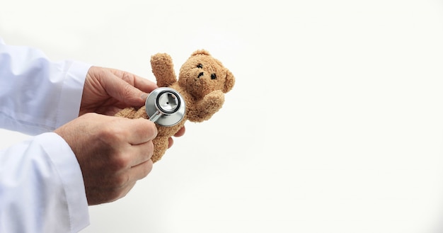 Les mains des médecins tenant un ours en peluche et plaçant le stéthoscope à proximité.