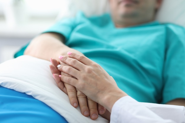 Photo les mains des médecins tiennent la main du patient allongé dans la salle