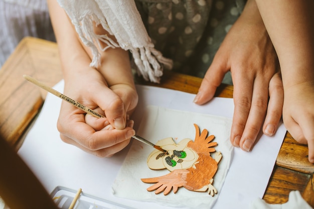 Photo mains de la mère et de l'enfant, qui dessinent ensemble avec un pinceau avec de la peinture sur un flan en bois. maman aide l'enfant à appliquer doucement la peinture.