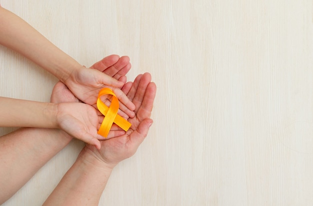 Les mains de la mère et de l'enfant tiennent un ruban orange sur fond blanc Journée mondiale de la sclérose en plaques