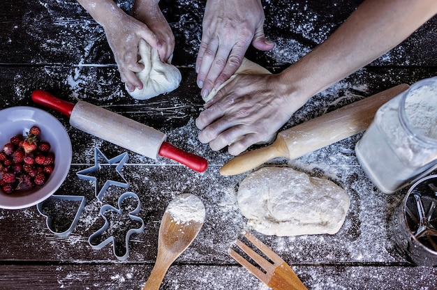 Des mains de mère et fille pétrir la pâte sur une table en bois. Préparation au four