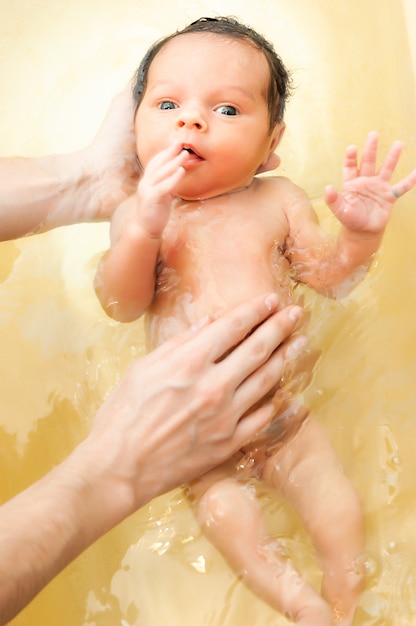 Les Mains D'une Mère Inconnue Et Prudente Tiennent Une Belle Petite Fille Aux Grands Yeux Drôles. Le Concept De Soins Et D'hygiène Sur Les Enfants. Les Enfants Et L'amour