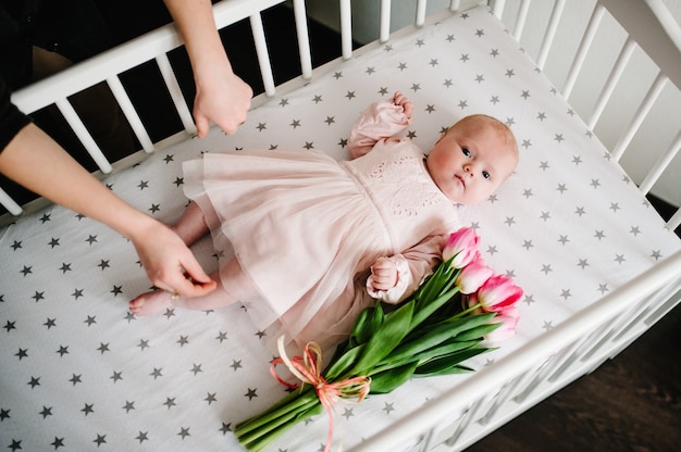 Mains de la mère qui prend un cadeau en vacances. Bébé nouveau-né avec bouquet de fleurs tulipes roses sur un lit. Fête des mères.