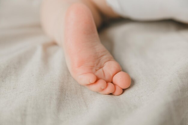 Les mains de la mère tiennent les jambes du bébé sur un lit de coton hygiène et soin et soin du talon du nouveau-né