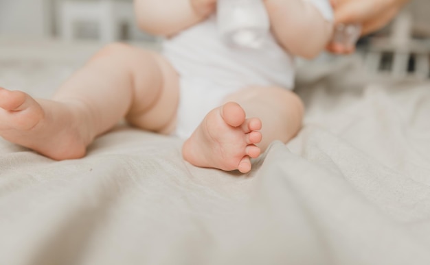 Les mains de la mère tiennent les jambes du bébé sur un lit de coton hygiène et soin et soin du talon du nouveau-né