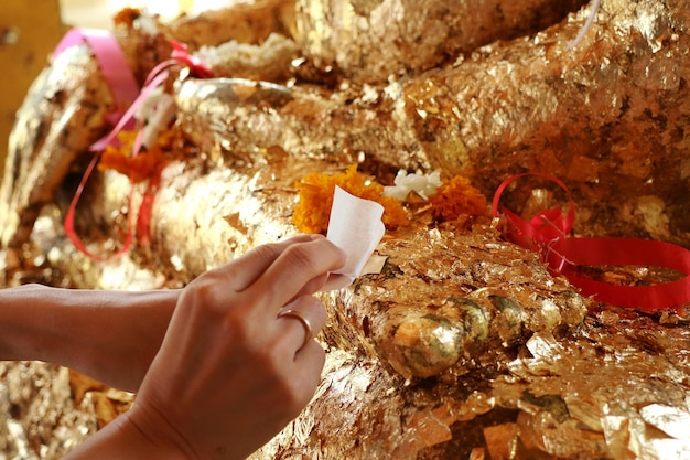 mains mettant la feuille d'or sur l'image de Bouddha. Concept de religion.