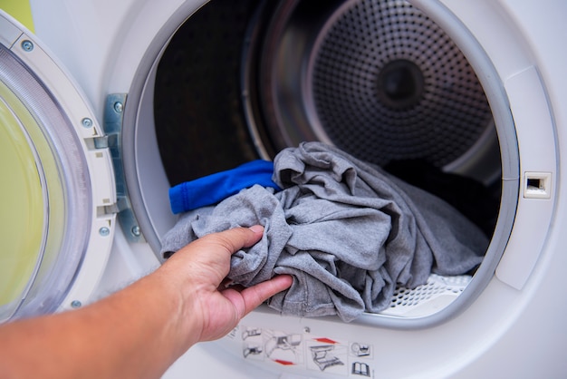 Les mains mettent les vêtements dans la machine à laver