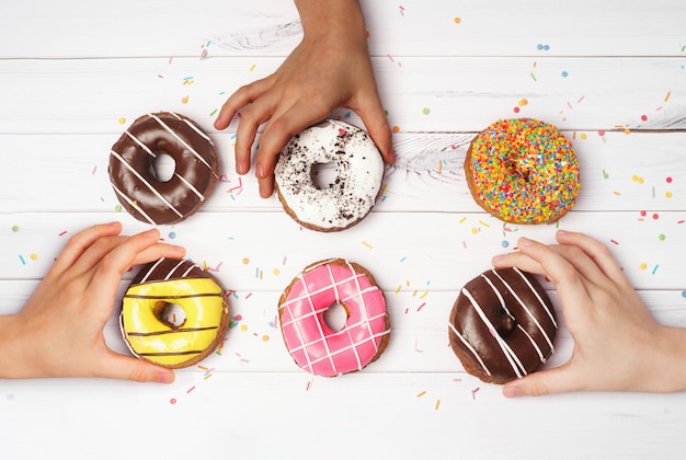 Les mains multiraciales prennent des beignets colorés.