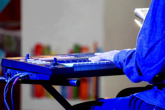 Mains de musicien jouant un clavier électronique sur scène avec un éclairage bleu