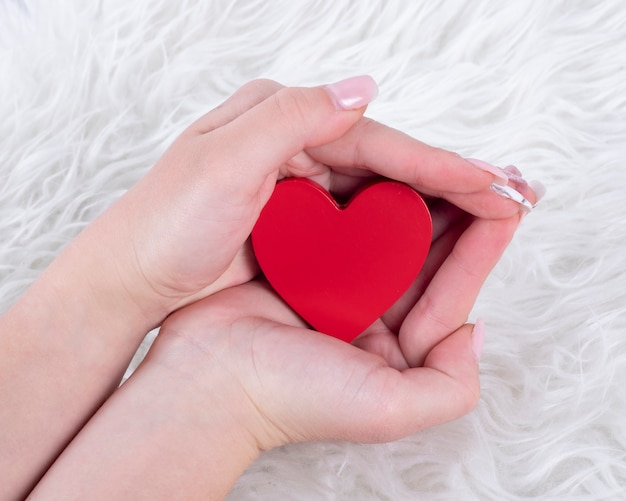 Mains avec des ongles en gel tenant un coeur rouge