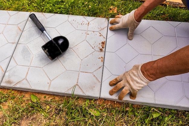 Les mains d'un ouvrier en gants posent des carreaux dans une maison de campagne Aménagement paysager pose de carreaux de pierre