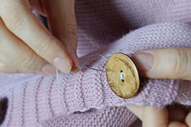 Les mains des ouvrières cousent un bouton en bois à une veste