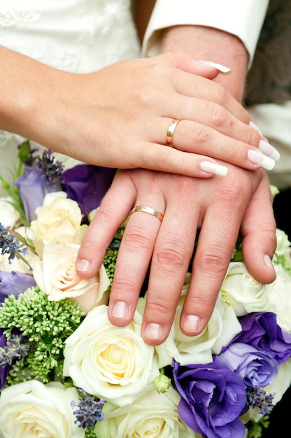 Mains de paire nuptiale avec des anneaux contre le bouquet de mariage