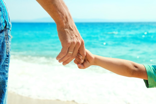 Mains d'un parent et d'un enfant heureux au bord de la mer lors d'un voyage dans la nature