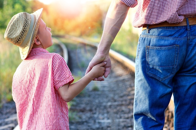 Mains de parent et fils en chapeau de cowboy près du chemin de fer avec valise