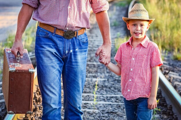 Mains de parent et fils en chapeau de cowboy près du chemin de fer avec valise