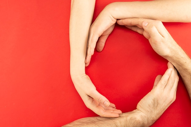 Les mains des parents et de l'enfant sont rassemblées en cercle avec une place pour le texte au centre sur un fond rouge.