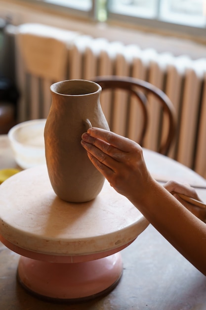 Les mains de passe-temps de poterie de céramiste professionnel travaillent sur un vase de potier en studio créent une cruche d'argile brute