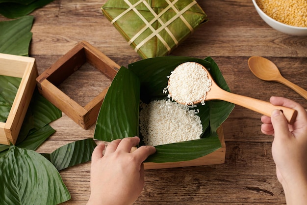 Mains d'une personne mettant du riz sous forme de bois avec des feuilles de lotus à l'intérieur lors de la préparation d'un gâteau pour la célébration du Têt