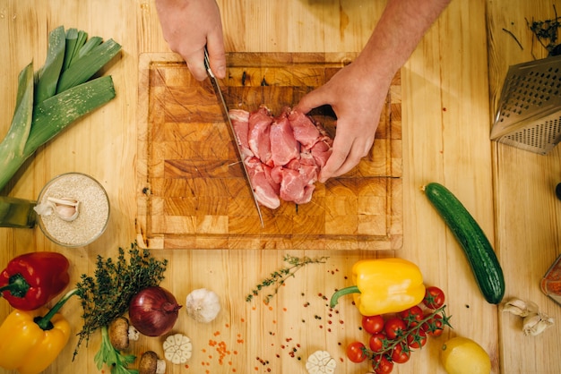 Mains de personne de sexe masculin avec couteau coupe la viande crue en tranches, vue du dessus
